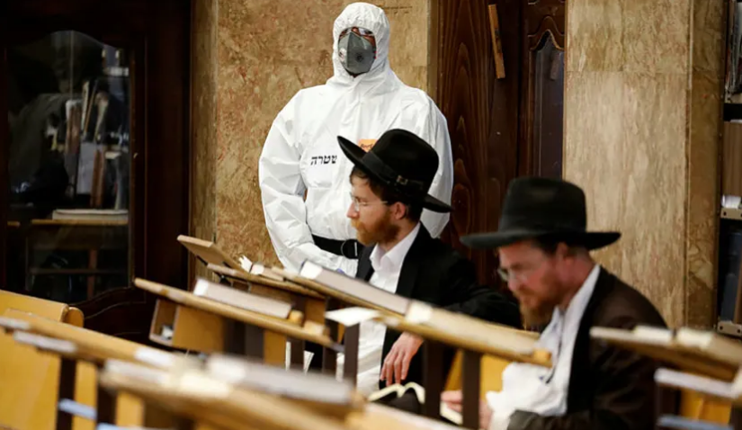 An Israeli police officer wearing protective gear waits to detain Ultra-Orthodox men as they pray in a synagogue, Bnei Brak, April 2, 2020.Credit: AP Photo/Ariel Schalit
