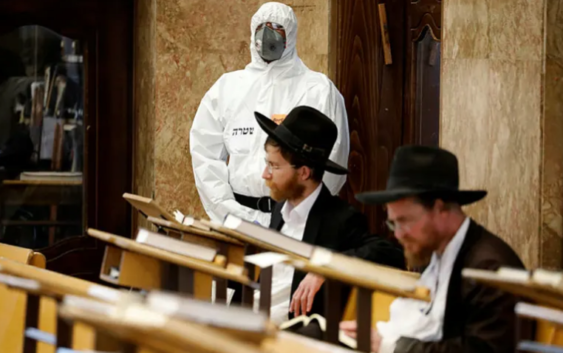 An Israeli police officer wearing protective gear waits to detain Ultra-Orthodox men as they pray in a synagogue, Bnei Brak, April 2, 2020.Credit: AP Photo/Ariel Schalit